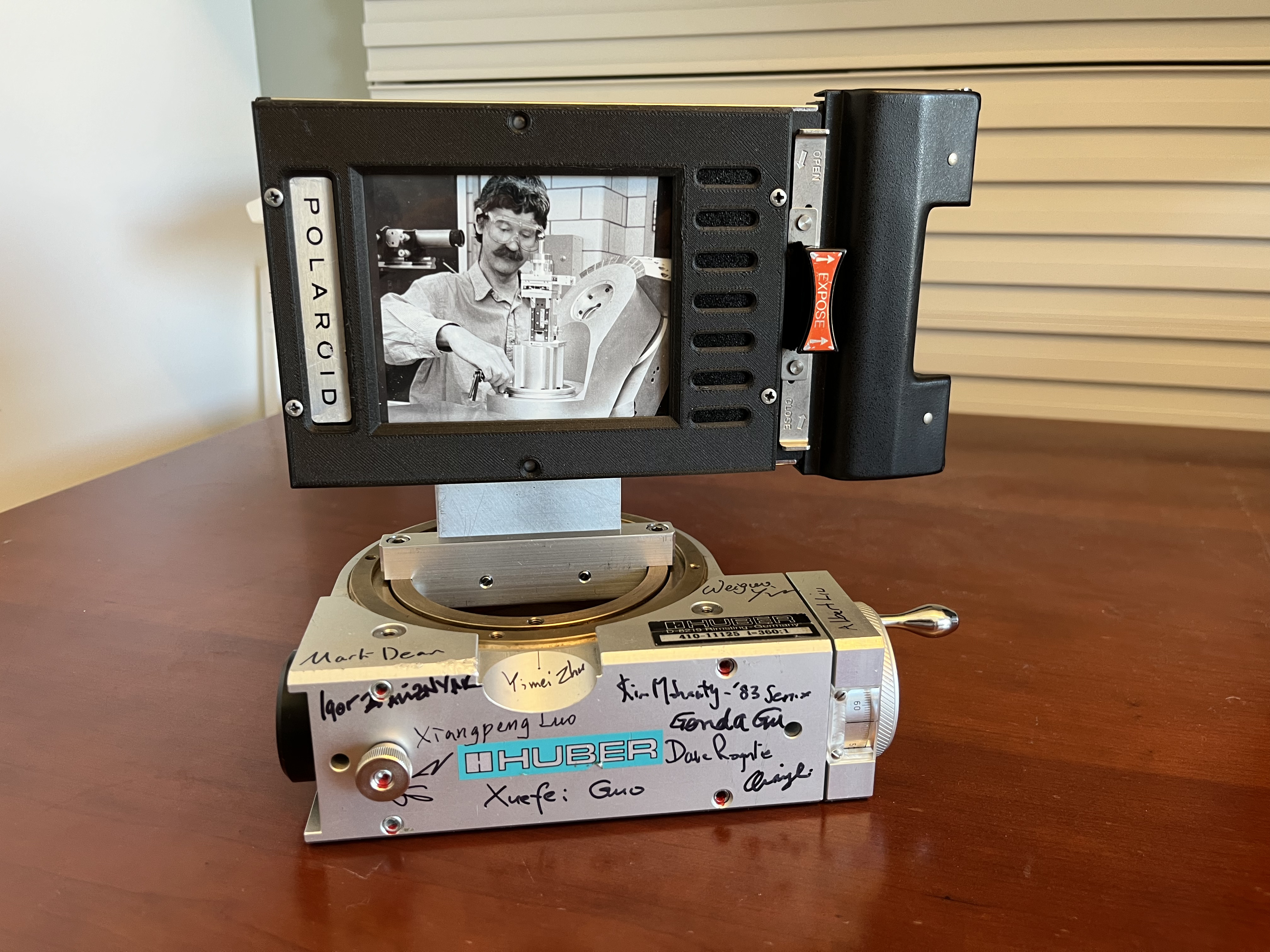 A signed Huber goniometer stage holding a Polaroid of Ian Robinson at a diffractometer
